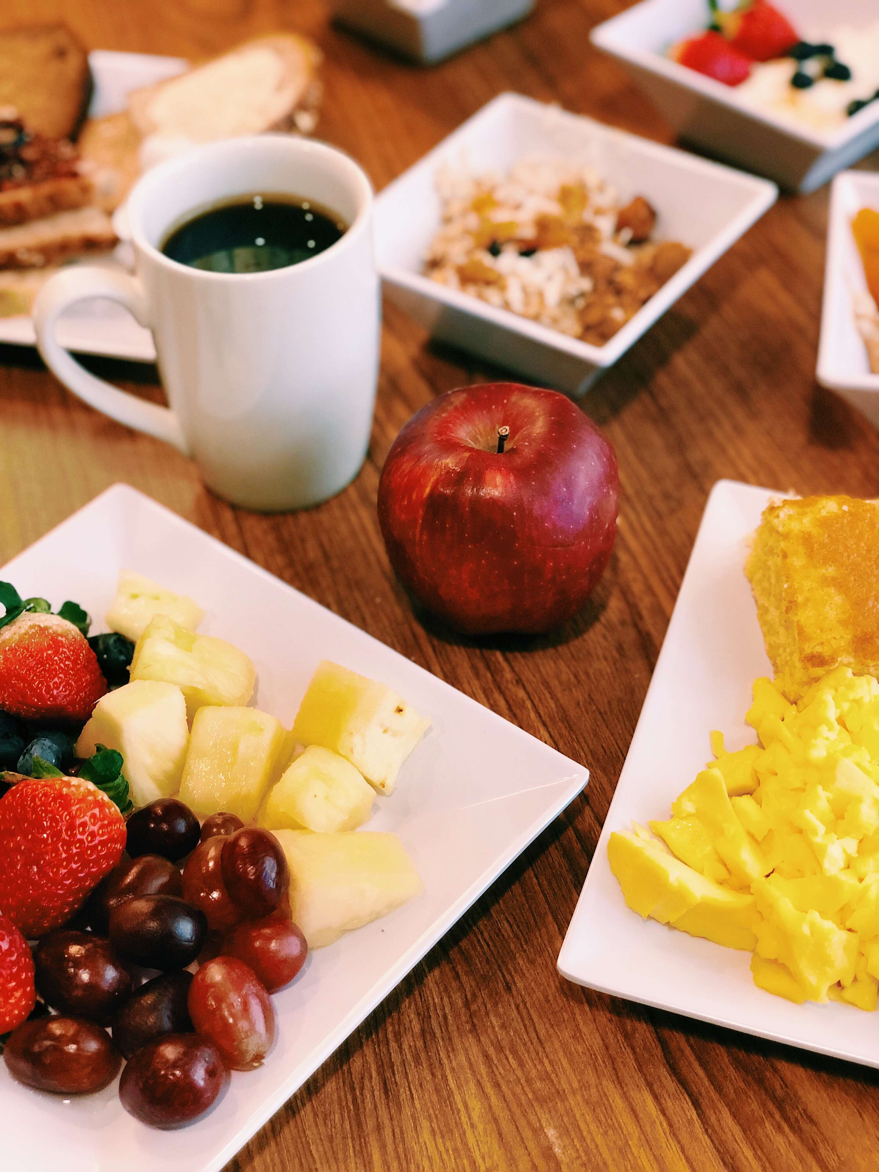 A breakfast table with plates of fruit, a cup of coffee, and a slice of toast.