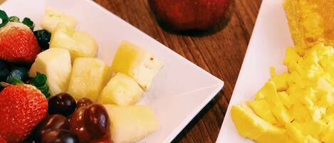A breakfast table with plates of fruit, a cup of coffee, and a slice of toast.