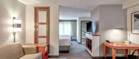 A hotel room with a sofa, a desk, a television, and a bed.