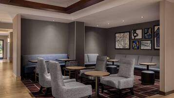 A modern lounge area with seating arrangements, including sofas and chairs, and a wall adorned with artwork.