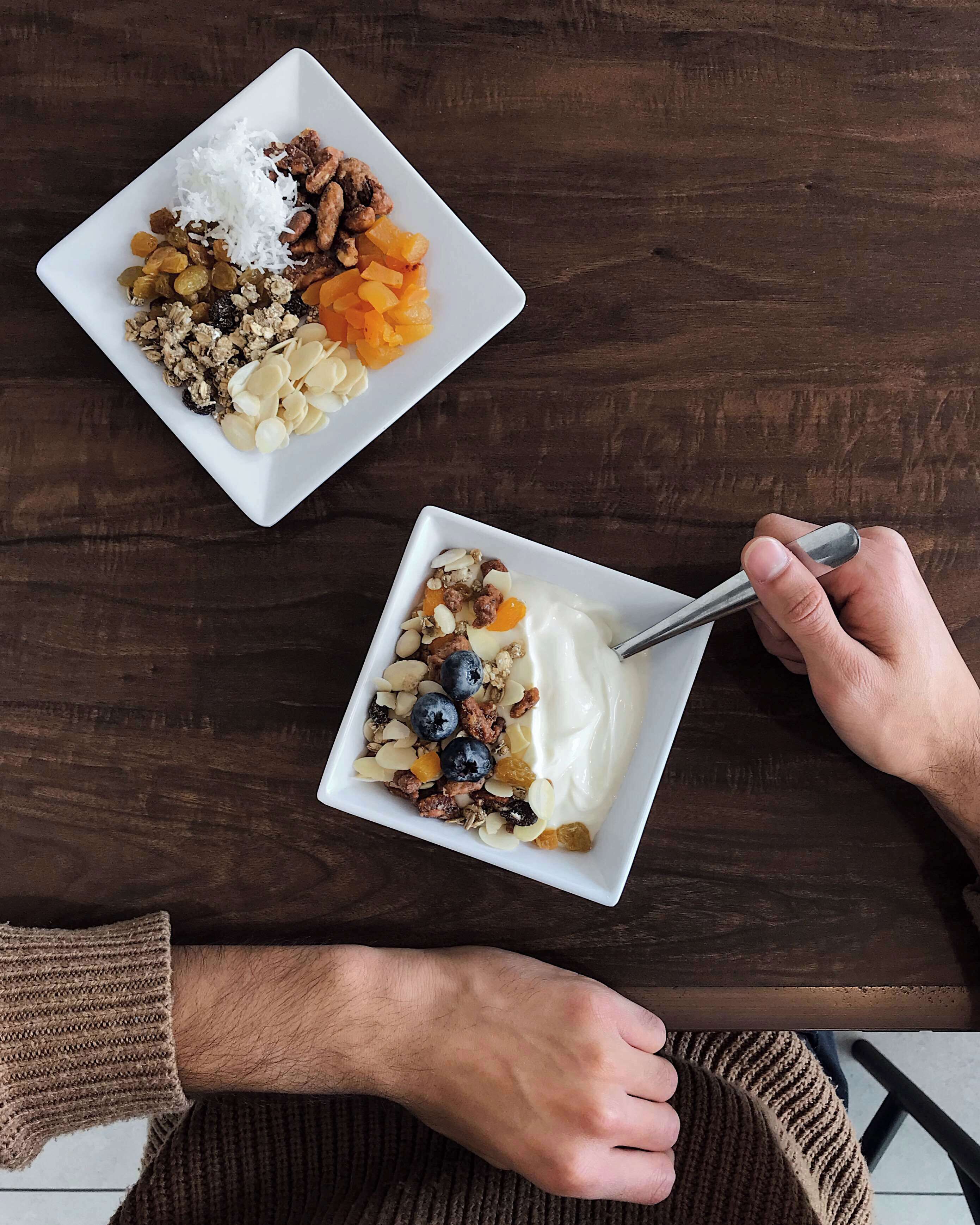 Dos tazones blancos de granola y yogur sobre una mesa de madera.