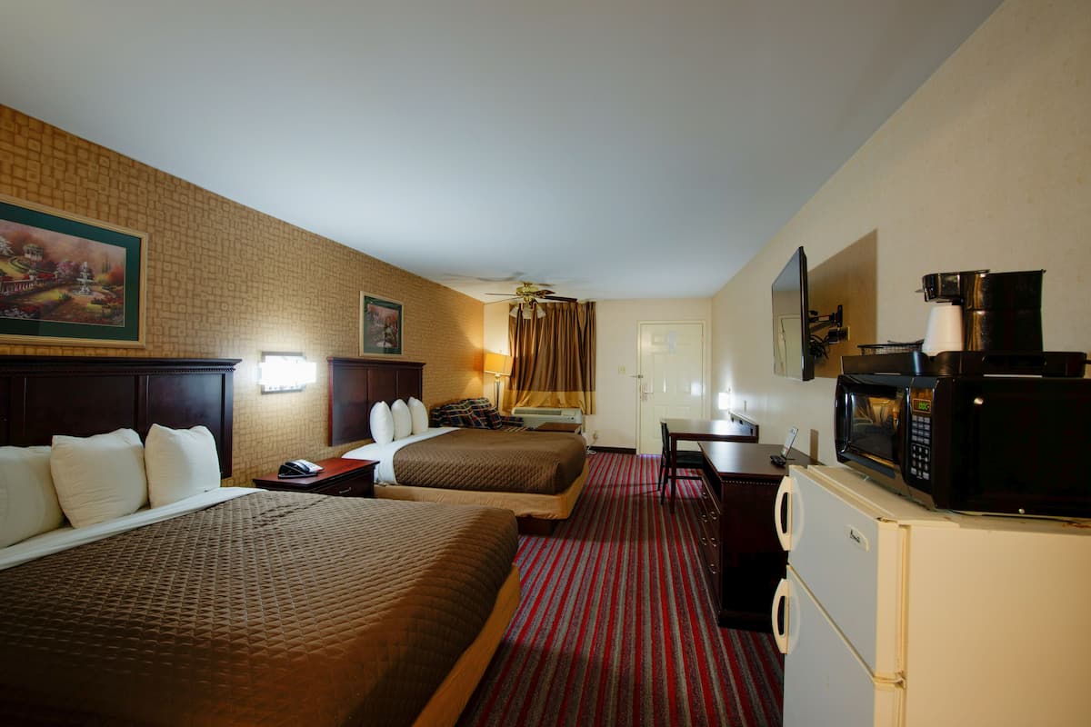 A hotel room with two beds, a desk, a refrigerator, and a microwave.