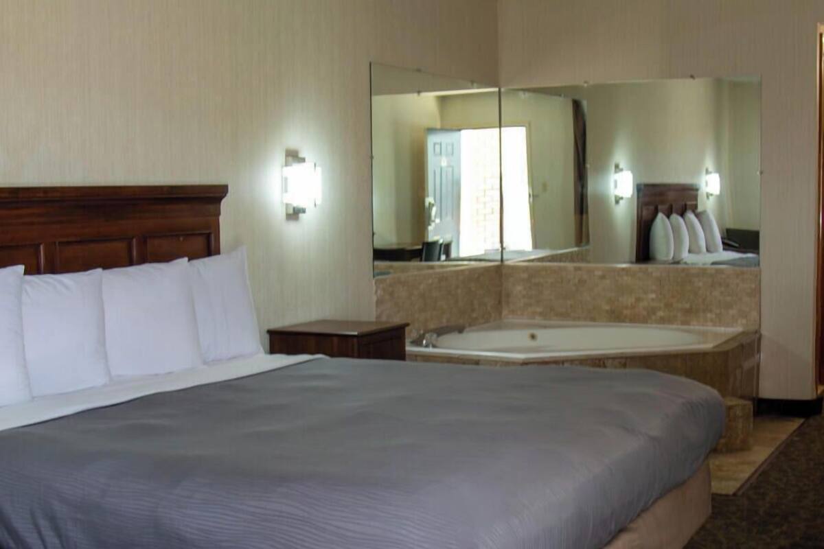 A hotel room with a large bed, a bathroom with a bathtub, and a mirror reflecting the room.