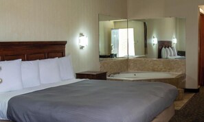 A hotel room with a large bed, a bathroom with a bathtub, and a mirror reflecting the room. - Brentwood Inn & Suites (Glen Allen)