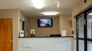 A hotel reception area with a flat-screen TV mounted on the wall, a reception desk, and a wooden door. - Brentwood Inn & Suites (Glen Allen)