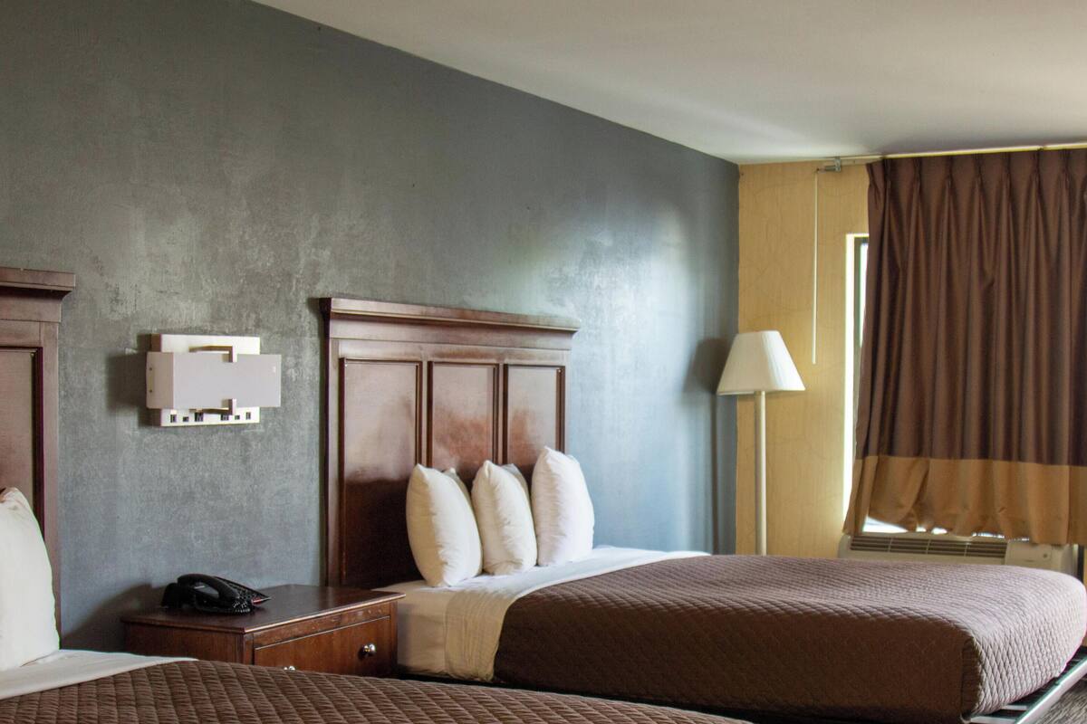 A hotel room with two beds, a bedside table with a phone, a lamp, and a window with curtains.