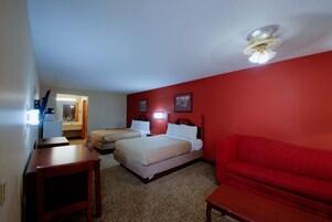 Una habitación de hotel con dos camas, un sofá rojo, una mesa de madera y un escritorio con una lámpara.