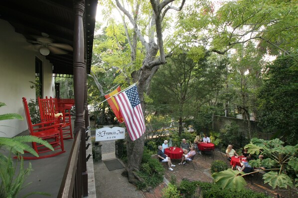 An outdoor seating area with tables and chairs, surrounded by trees and greenery.