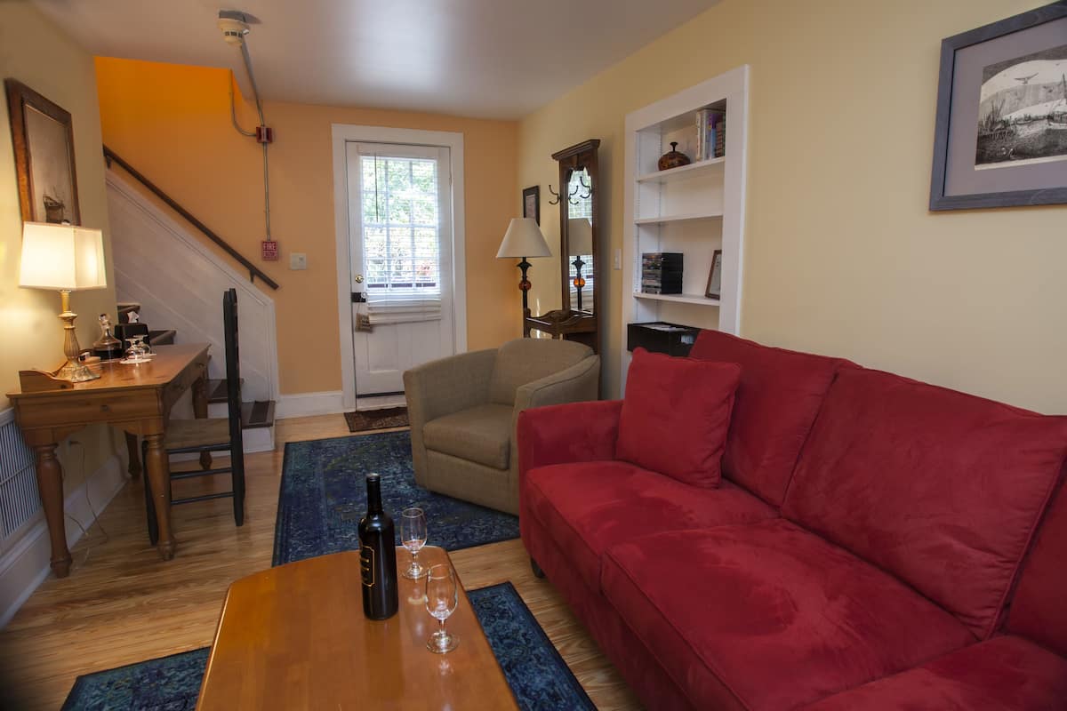 A living room with a red sofa, wooden coffee table, and a lamp. There is a chair, a bookshelf, and a door with a window.