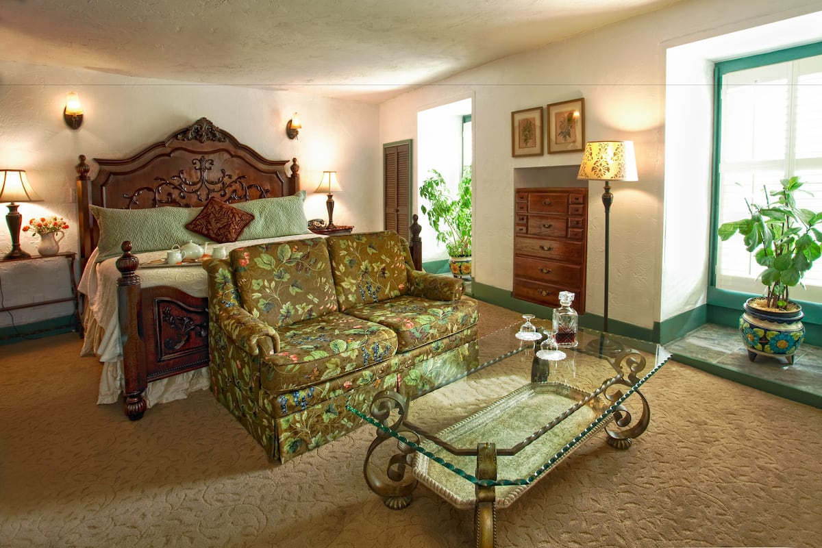 A bedroom with a bed, a floral sofa, a glass coffee table, and a dresser.
