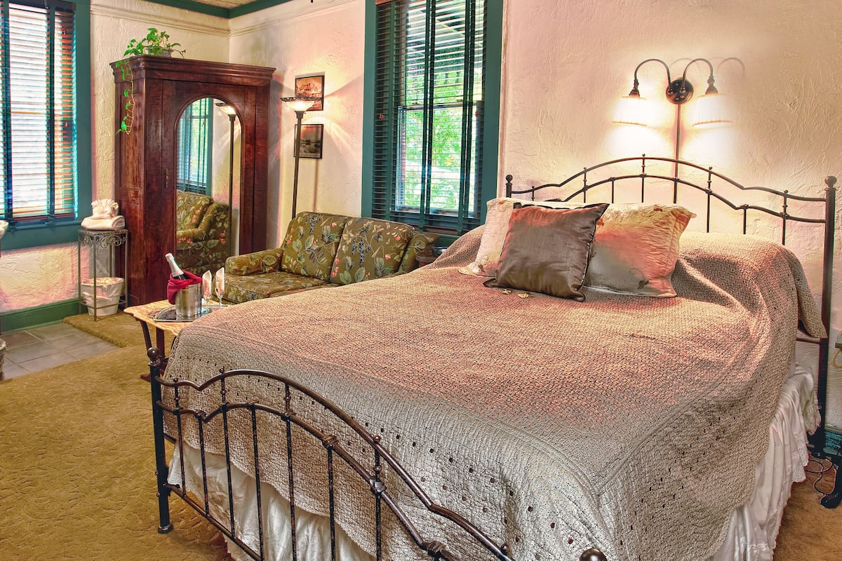 A bedroom with a large bed, a wooden cabinet, a sofa, and a mirror.