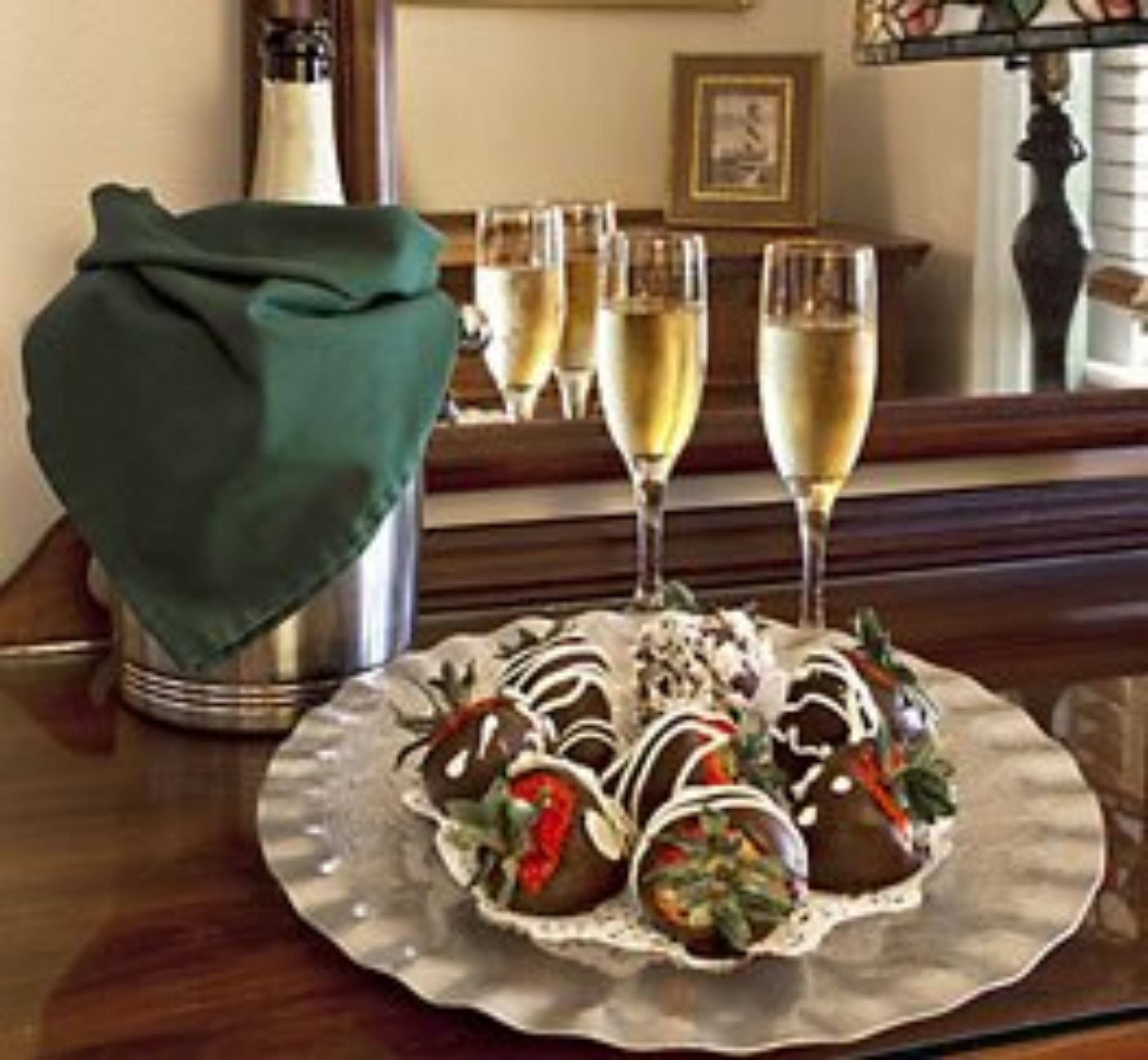 A plate of chocolate-covered strawberries on a glass table with a green cloth and two champagne flutes.
