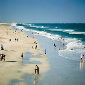 A crowded beach with people walking and swimming.