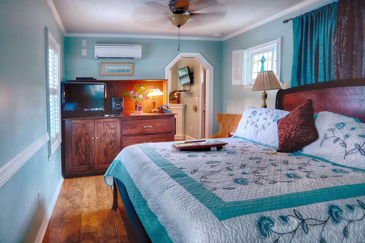 A bedroom with a bed, a dresser, a television, and a window with curtains.