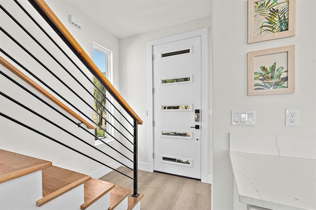 A modern staircase with wooden steps and black railings, leading to a white door with multiple panels.