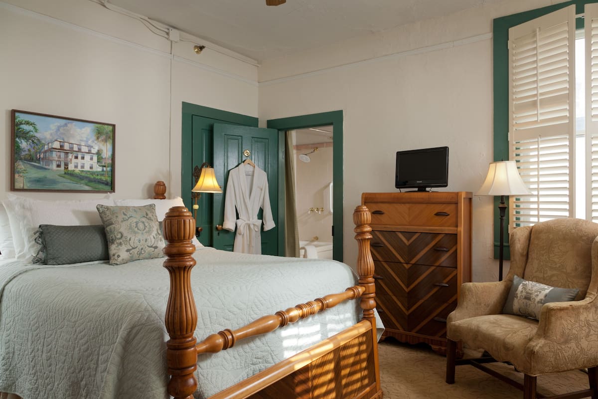 A bedroom with a bed, a chair, a dresser, a television, and a painting on the wall.