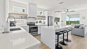 Une cuisine moderne avec des meubles blancs, des appareils en acier inoxydable et un îlot central doté de tabourets de bar.