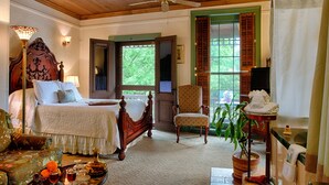 Une chambre avec un plafond en bois, un lit recouvert d’une courtepointe blanche, une chaise, une table avec une lampe et une plante en pot.