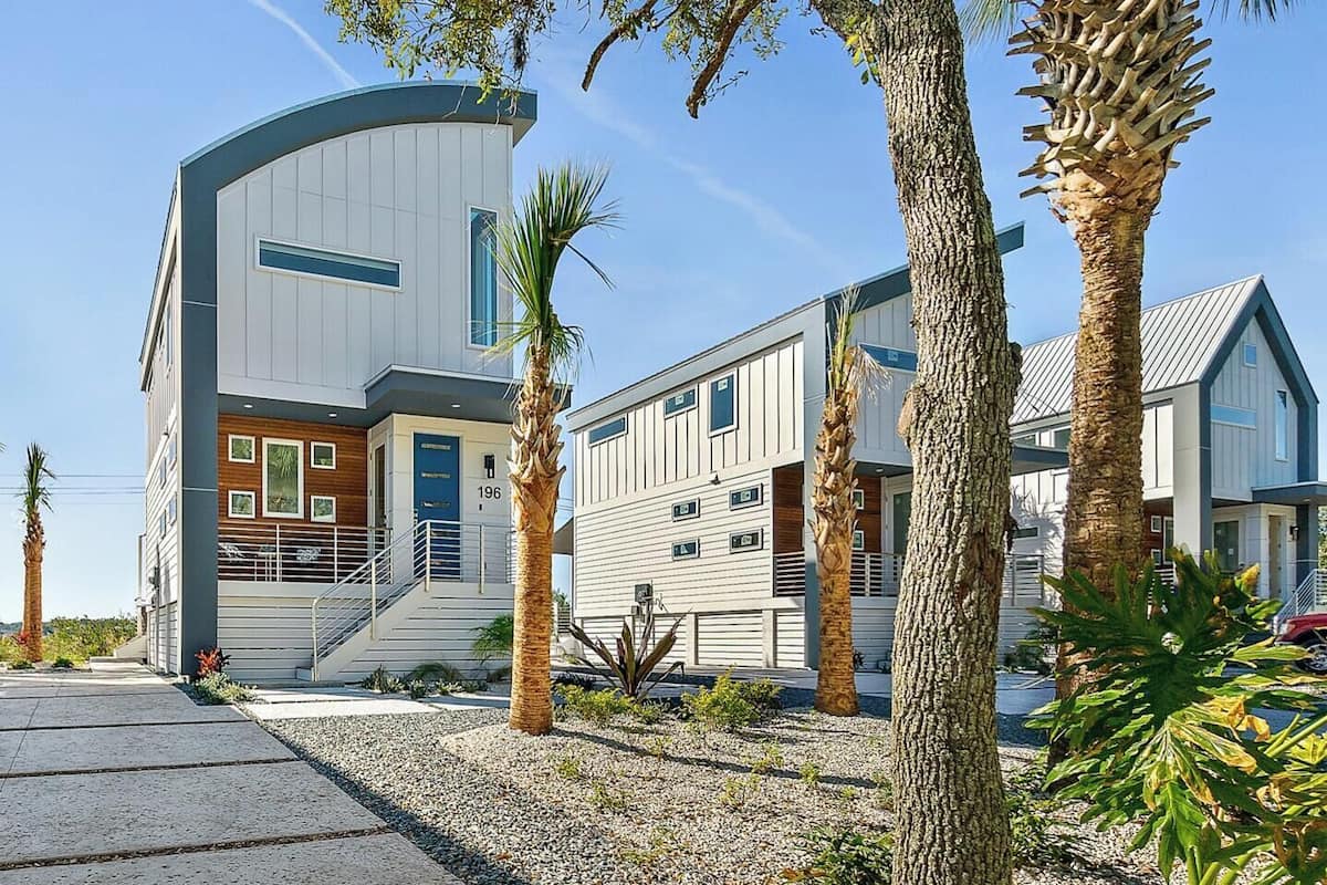 A modern residential building with a curved facade, a central entrance with a staircase, and a well-maintained garden with palm trees.