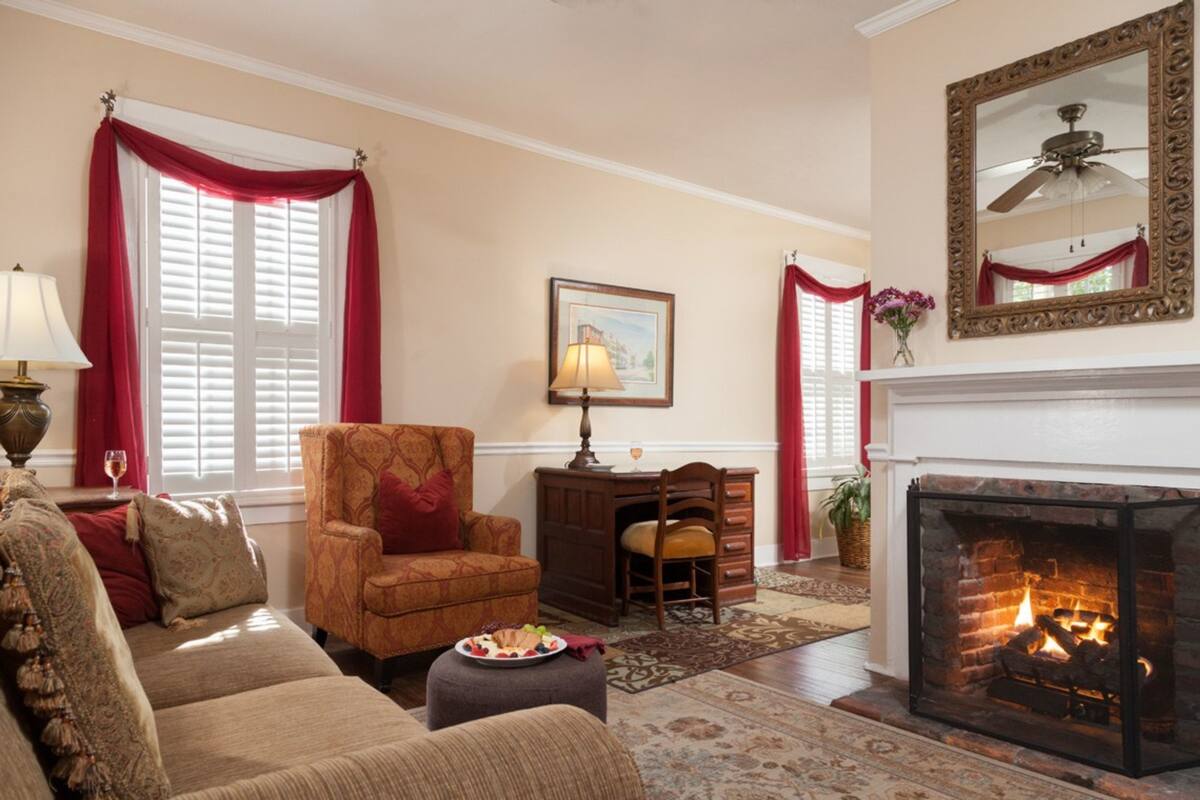 A cozy living room with a fireplace, a sofa, a chair, a desk, and a lamp.