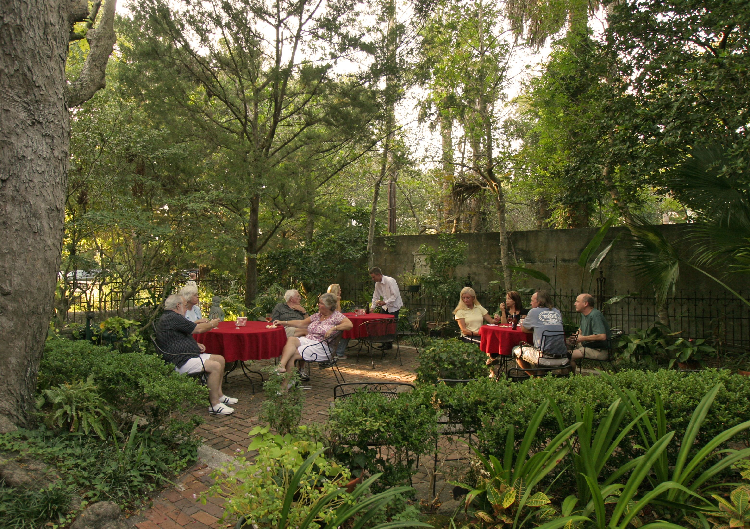 Un grupo de personas sentadas en mesas en un jardín al aire libre, con abundante vegetación y árboles.
