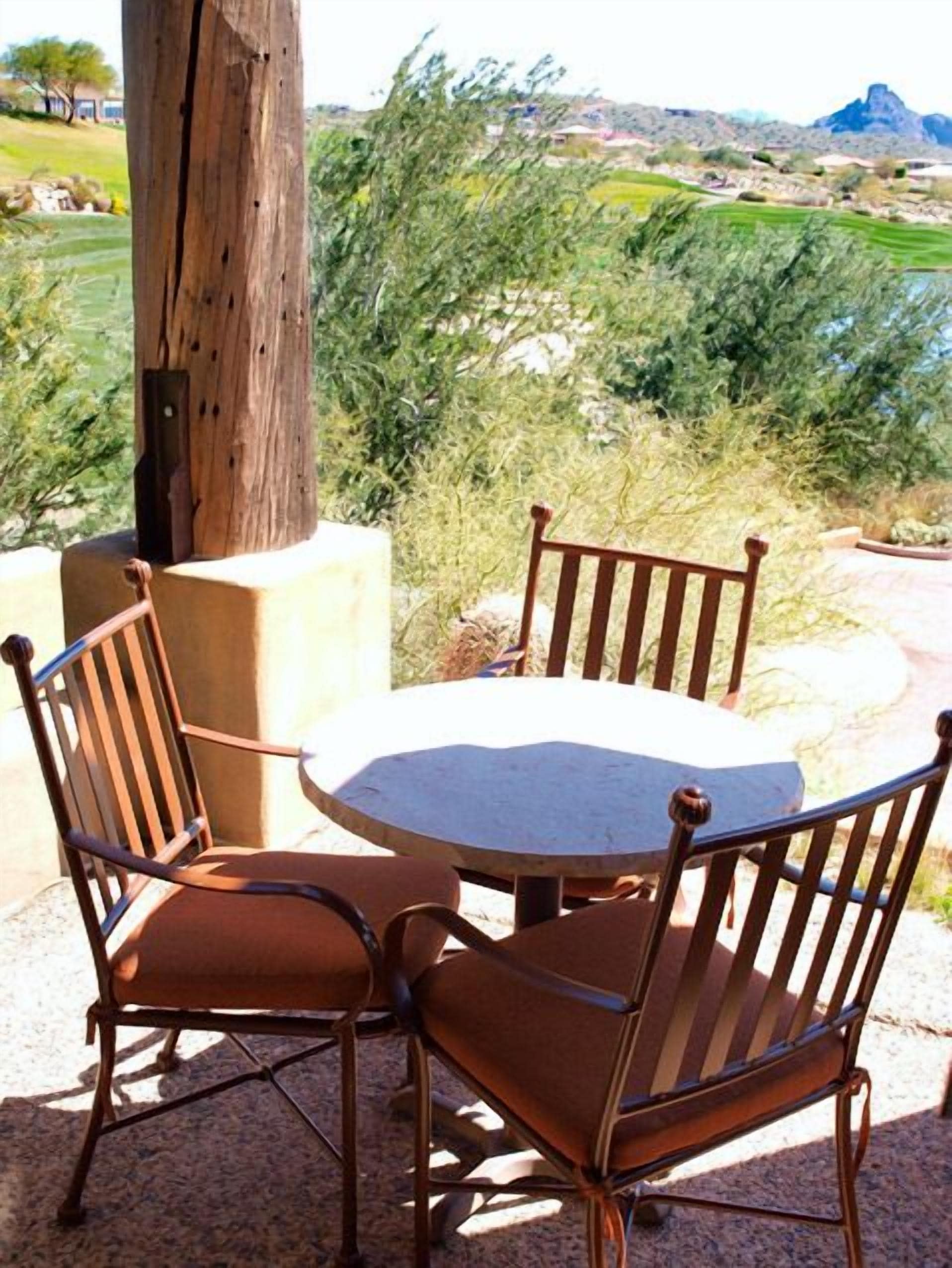 A round table with four chairs, set outdoors with a view of a mountainous landscape.
