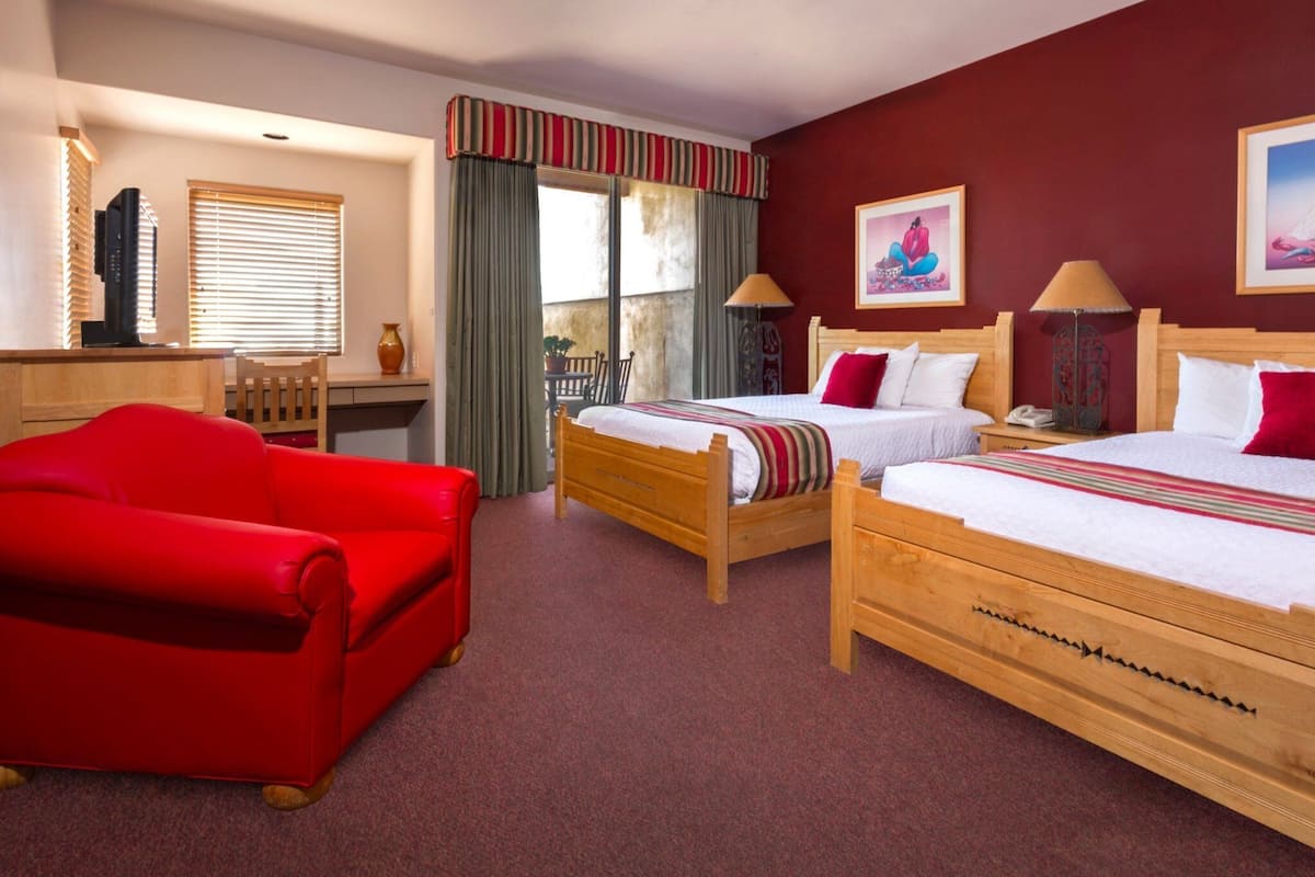 A hotel room with two wooden beds, a red sofa, a desk, and a window with blinds.