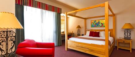 A four-poster bed with a wooden frame, a red sofa, a lamp, and a painting on the wall.