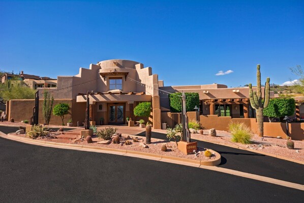 A desert-style building with a curved facade, a central entrance, and a landscaped courtyard with cacti and small trees. - Inn at Eagle Mountain (Fountain Hills)