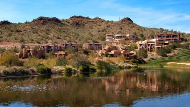 A cluster of modern, multi-story buildings with a river in the foreground.