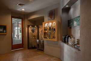 Un pasillo con suelo de baldosas de piedra, una puerta de madera, una vitrina con varios objetos y una máquina de café sobre una encimera.