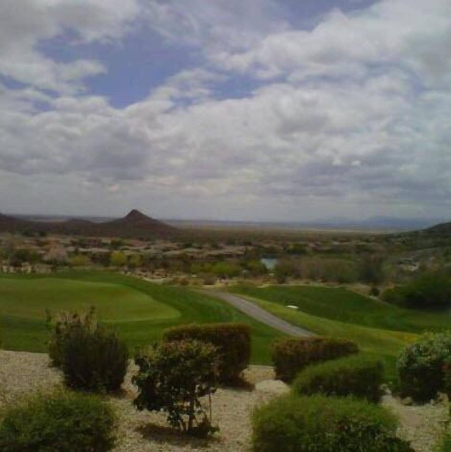Camp de golf sota un cel blau, amb turons suaus i una muntanya a la distància.