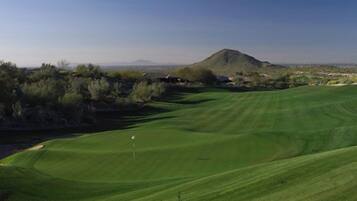 A golf course with a flagstick, rolling green hills, and distant mountains.