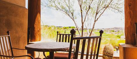 A patio with a table and chairs, a cactus, and a view of a green landscape.