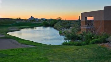 A golf course with a water hazard, a building with a flat roof, and a clear sky.