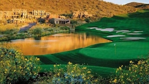 A golf course with a pond, a clubhouse, and a hilly backdrop.
