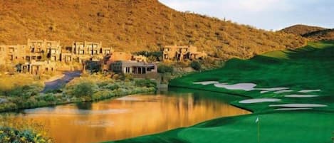 A golf course with a pond, a clubhouse, and a hilly backdrop.