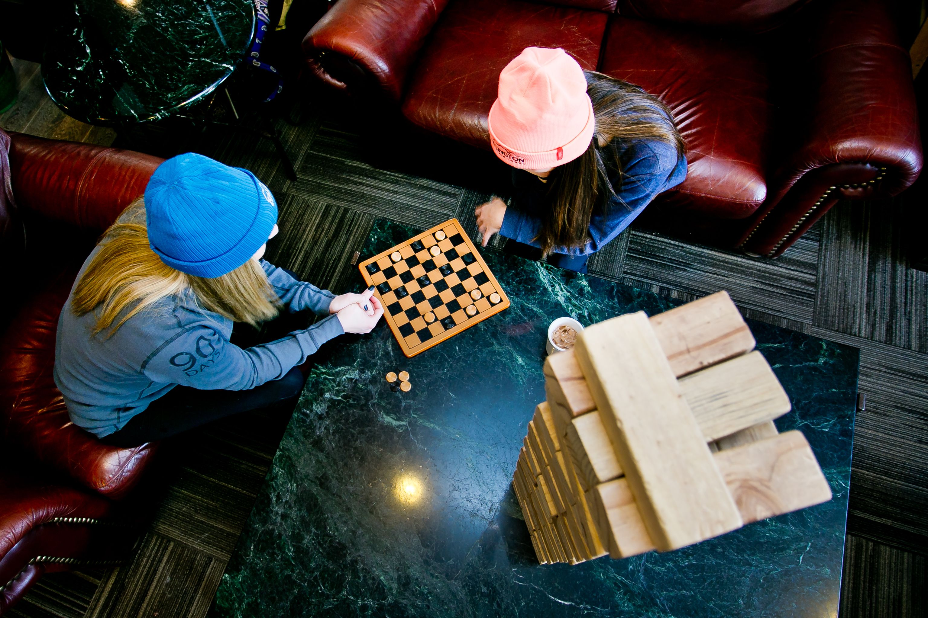 Dos personas jugando ajedrez sobre una mesa de mármol en una habitación con muebles de cuero.