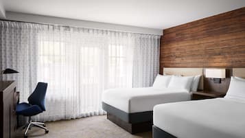Habitación de hotel con dos camas, un escritorio, una silla y un ventanal con cortinas translúcidas.