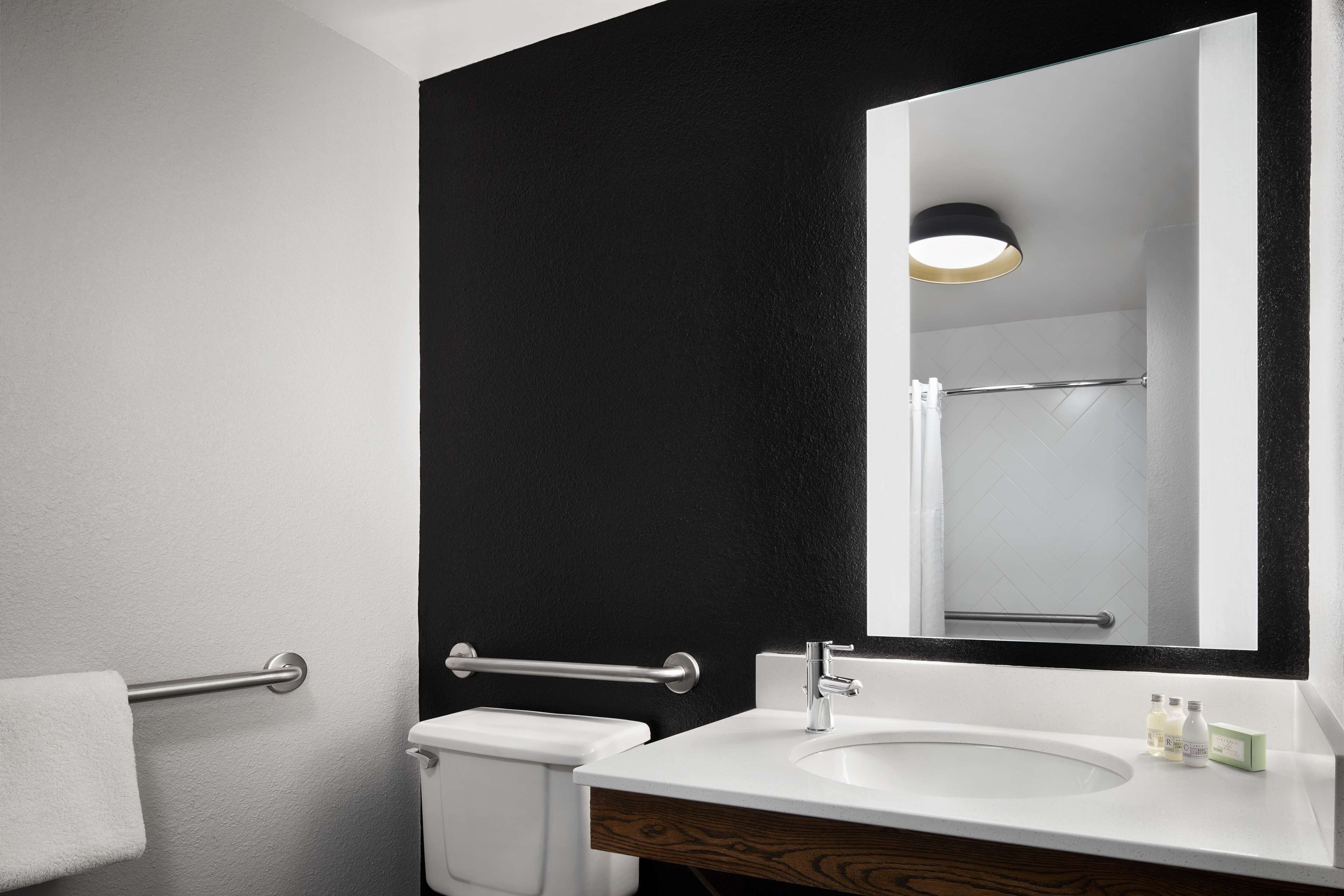 Une salle de bain moderne avec un lavabo blanc, un grand miroir et un mur d’accent noir.