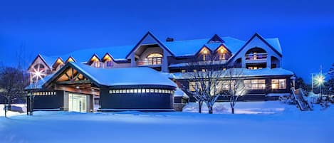 A large, multi-story building with a snow-covered roof and multiple illuminated windows.