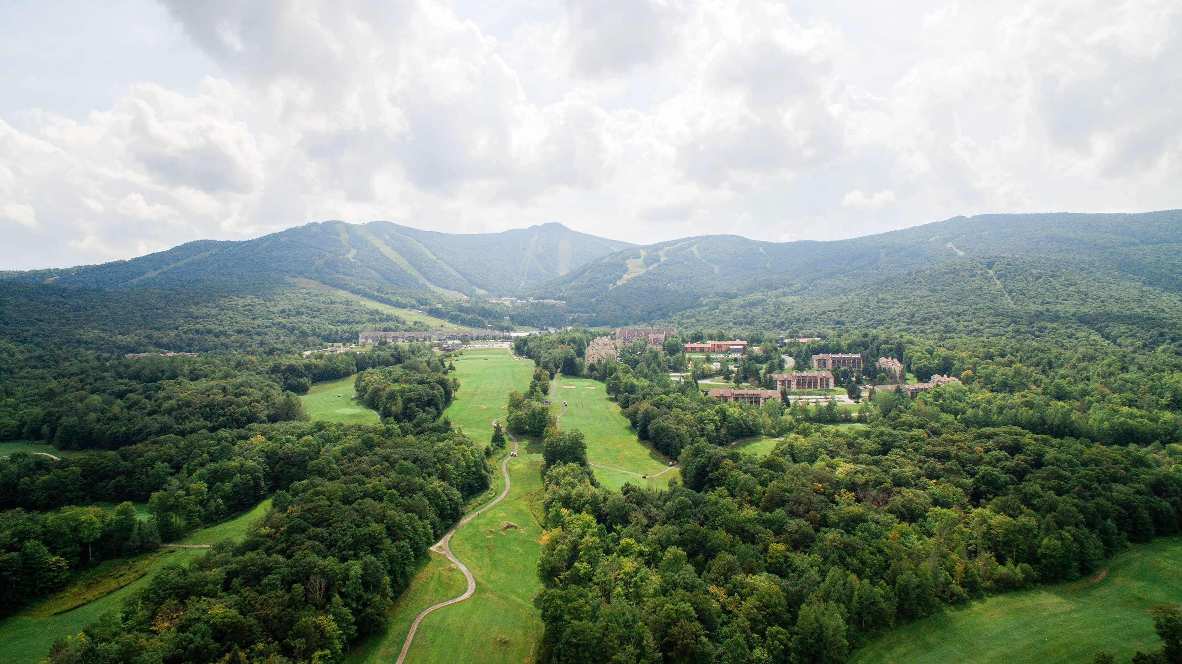 Un parcours de golf doté d’un club-house et de bâtiments entourés de collines boisées.
