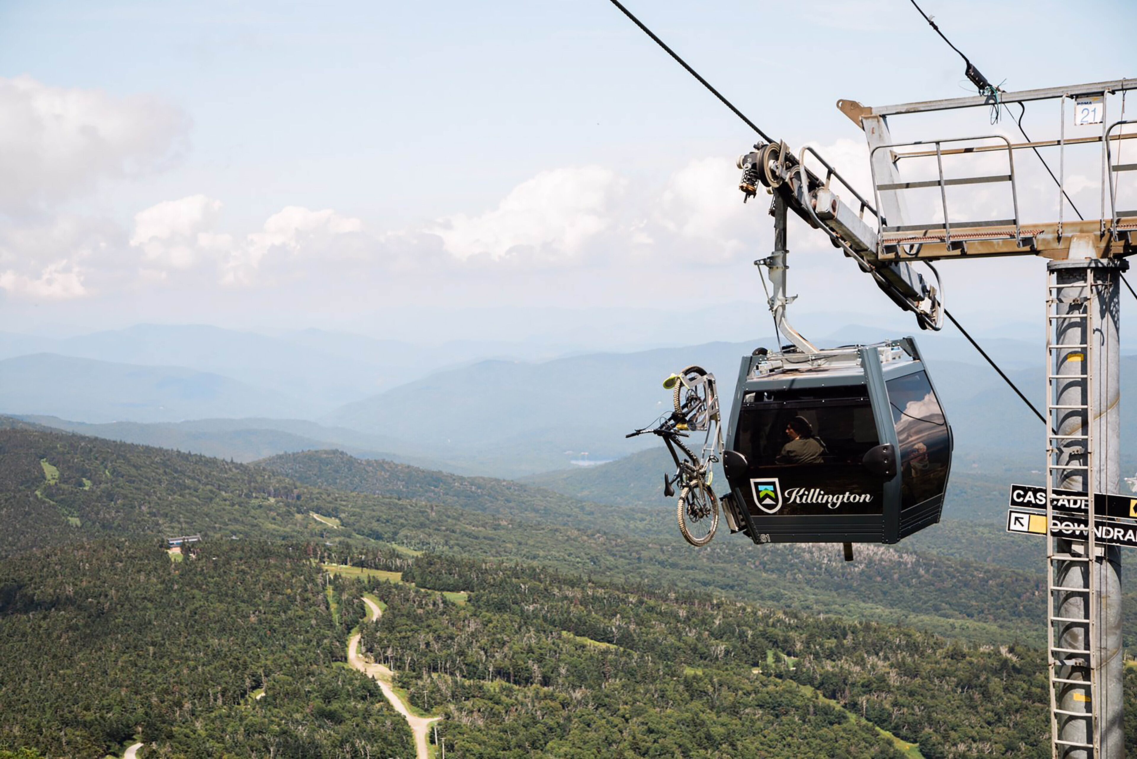 A cable car with "Killington" branding, suspended over a mountainous landscape with a clear sky.