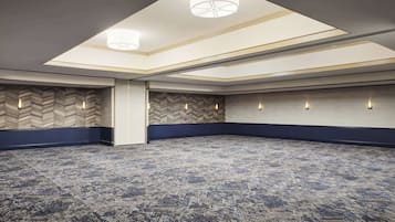 A large, empty conference room with a patterned carpet, a high ceiling with skylights, and wall-mounted lighting.