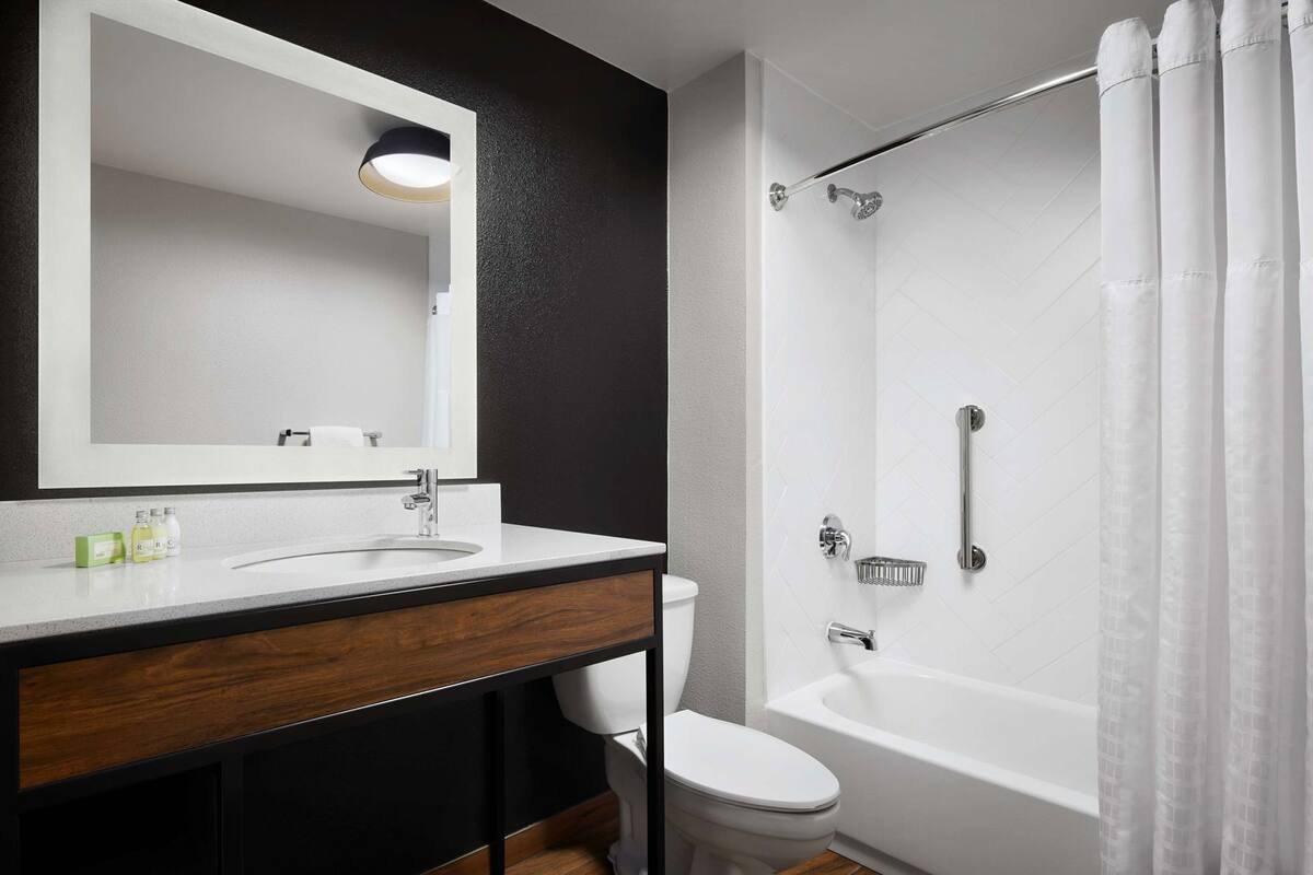 A bathroom with a white sink, mirror, and toilet, a shower with a glass door, and a wooden vanity.