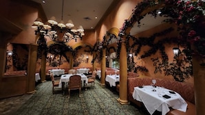 A restaurant with tables and booths, a patterned carpet, and decorative arches with vines.