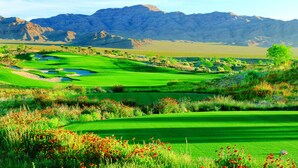 A golf course with a desert landscape and mountains in the background.