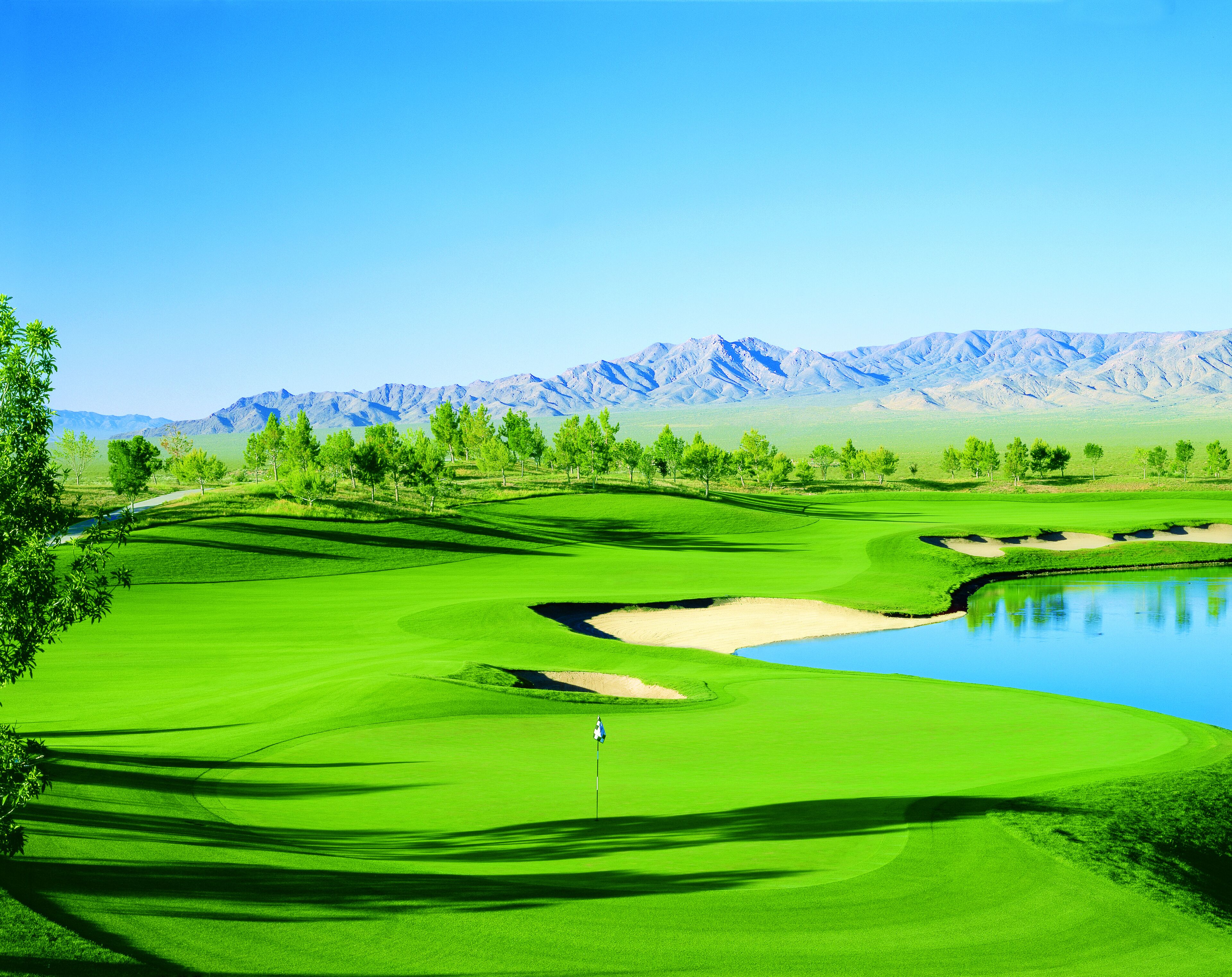 Un parcours de golf avec des obstacles d’eau, des arbres et des montagnes en arrière-plan.