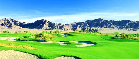 A golf course with sand bunkers and a mountainous backdrop.