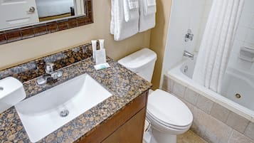 A bathroom with a granite countertop sink, a toilet, and a bathtub.